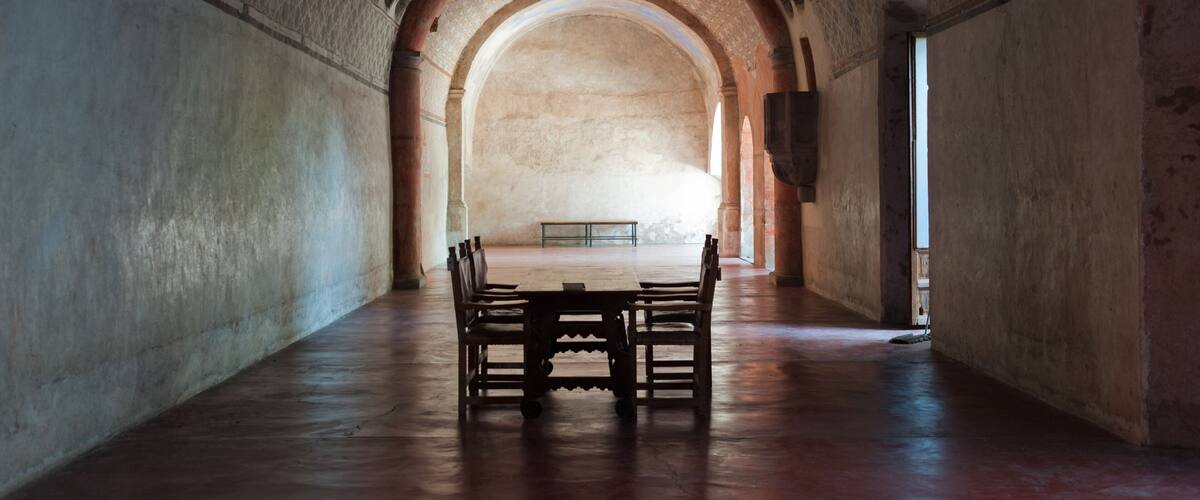A corridor with a wooden table and chairs, arched ceiling, and patterned walls.