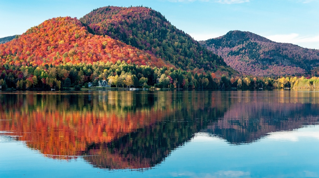 The hills covered with red maple forests are reflected in a lake in Quebec on a beautiful autumn evening
