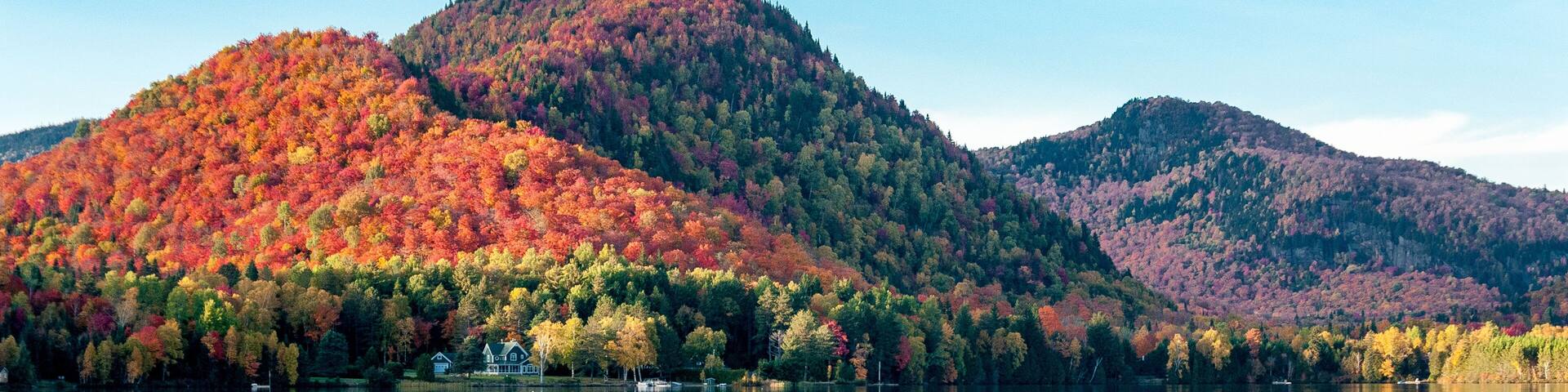 The hills covered with red maple forests are reflected in a lake in Quebec on a beautiful autumn evening