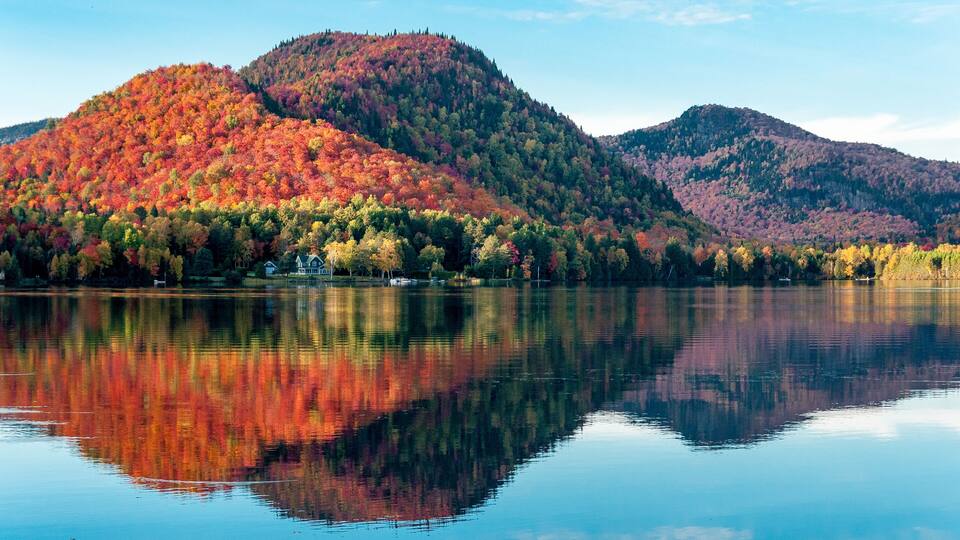 A calm lake with a reflection of a forested mountain range in autumn colors.