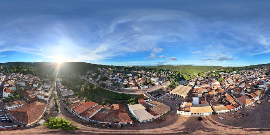 Vista panorâmica de uma cidade histórica com edifícios de telhados em terracota, uma praça central e colinas ao redor.
