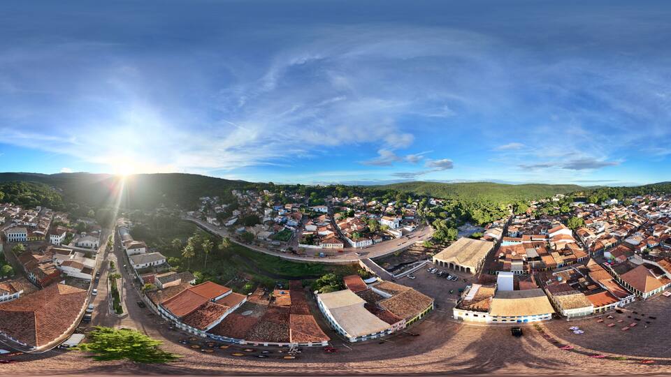 A panoramic view of a historic town with terracotta-roofed buildings, a central square, and surrounding hills.