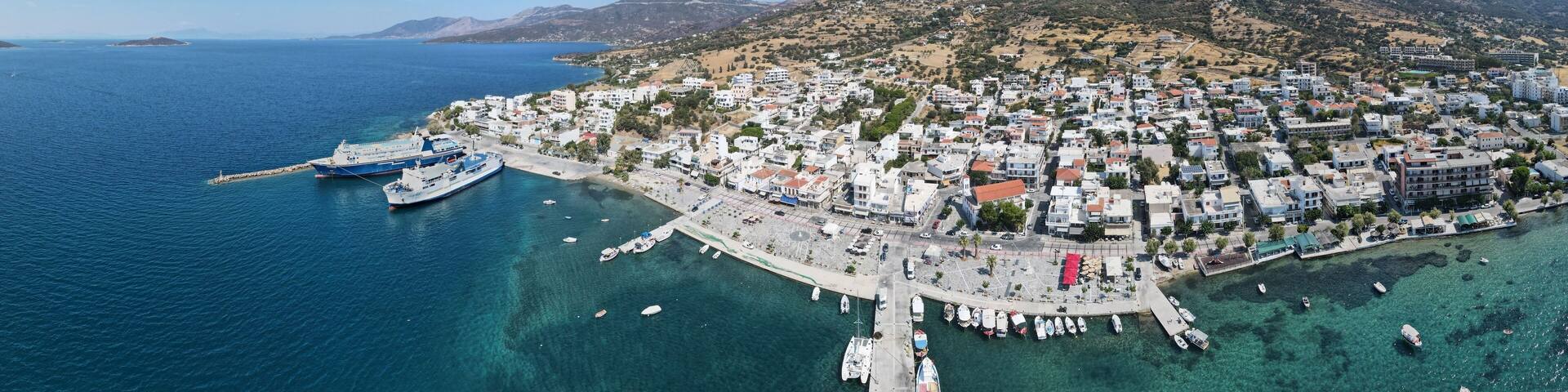 Wide-angle shot of the Marmari coast harbor during daytime with a clear blue sky, Greece