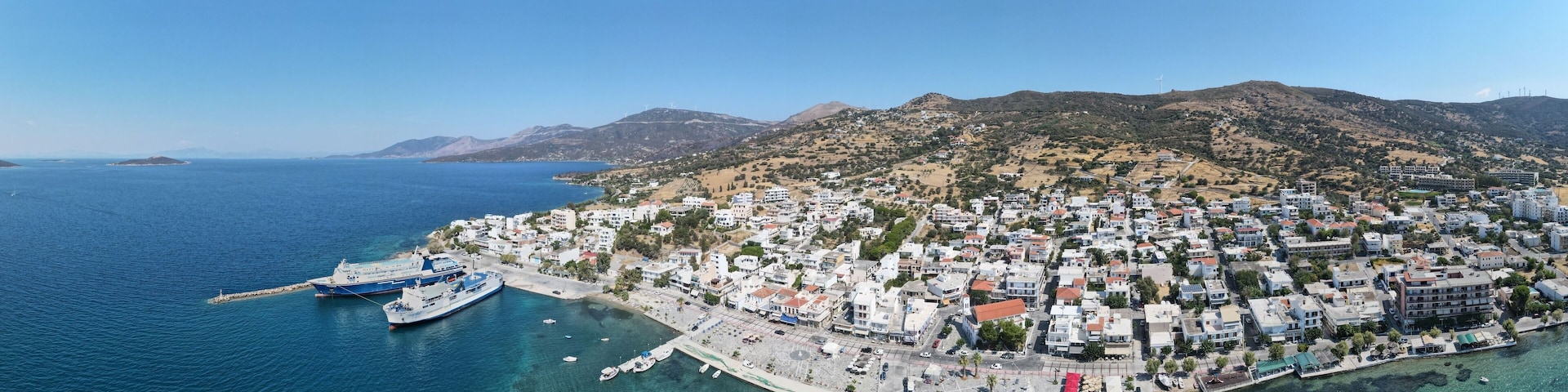 Wide-angle shot of the Marmari coast harbor during daytime with a clear blue sky, Greece