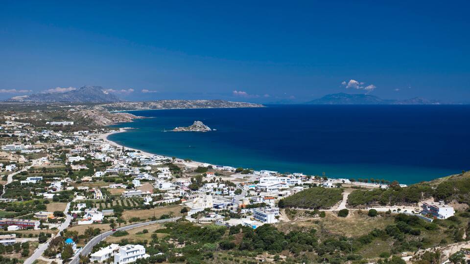 A coastal town with a beach, buildings, and a mountain in the background.