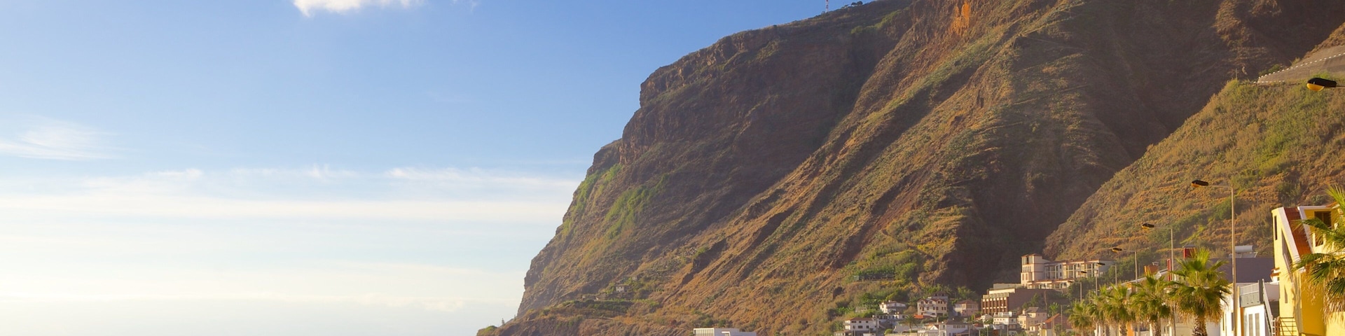 Una carretera costera con un acantilado pronunciado, olas del océano y una hilera de edificios a la orilla del mar.