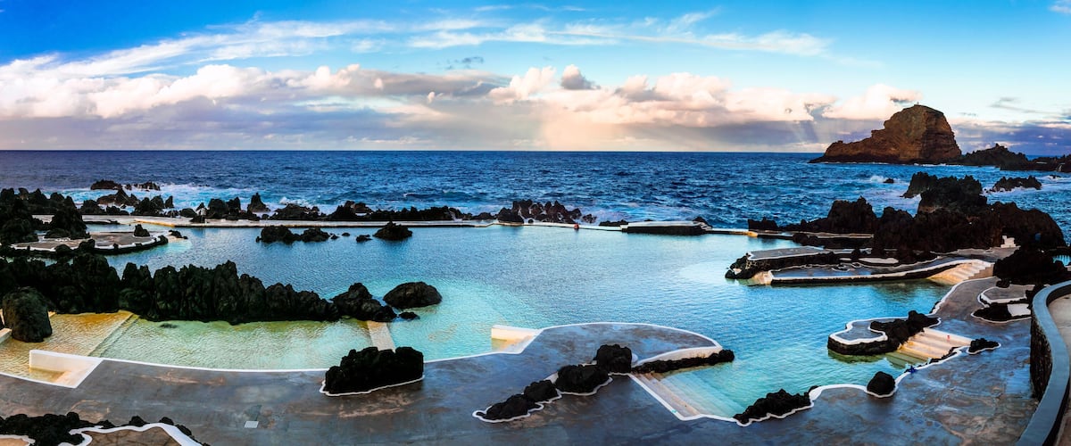 A coastal resort with a large pool surrounded by rocky formations and a prominent rock formation in the background.