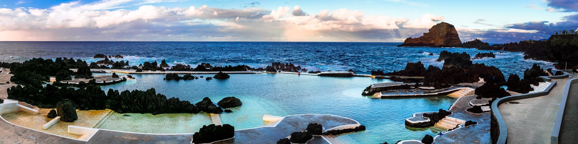A coastal resort with a large pool surrounded by rocky formations and a prominent rock formation in the background.