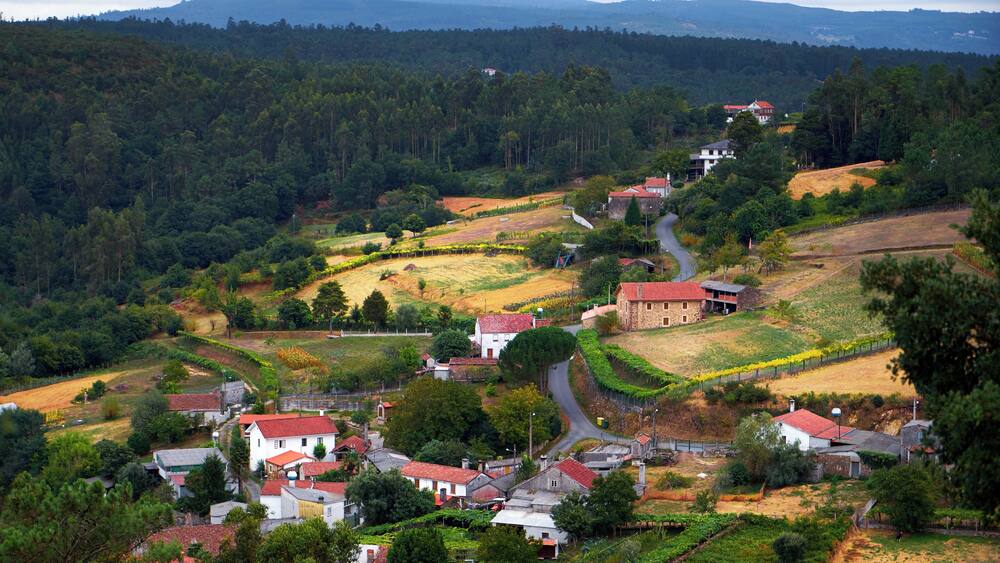 A rural village with terraced vineyards, stone houses, and rolling hills in the background.
