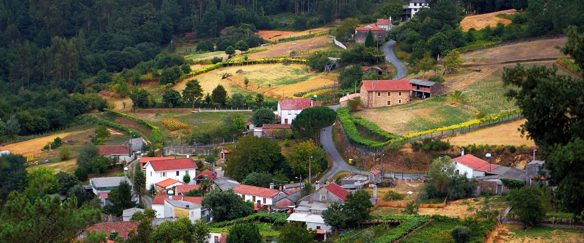 A rural village with terraced vineyards, stone houses, and rolling hills in the background.