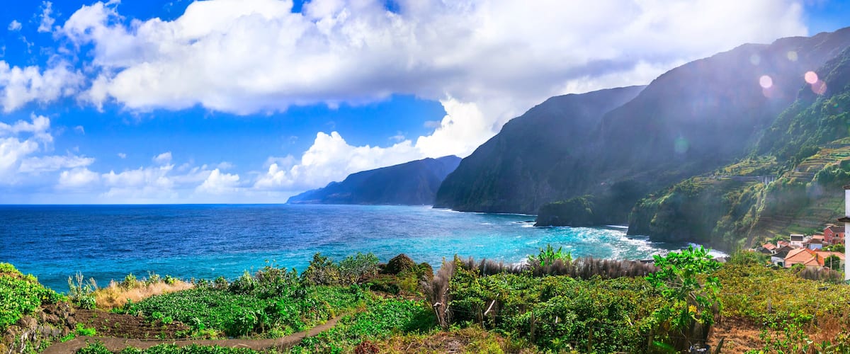 A coastal village with terraced fields, a clear blue sea, and a mountain backdrop.