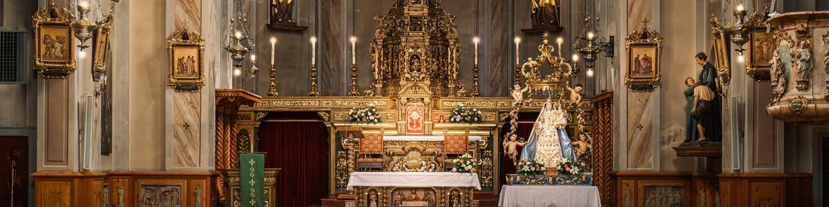 An ornate church interior with a central altar, statues, and a large chandelier.