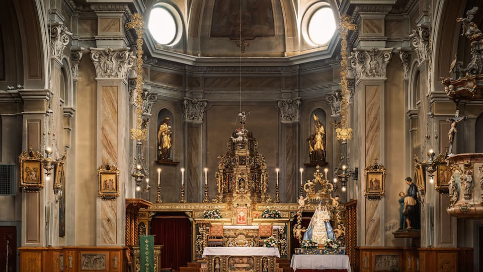 The interior of the St. Mary Parish Church in Livigno, Italy, featureing beautifully ornated altar, decorations and lit candles that create an serene atmosphere.