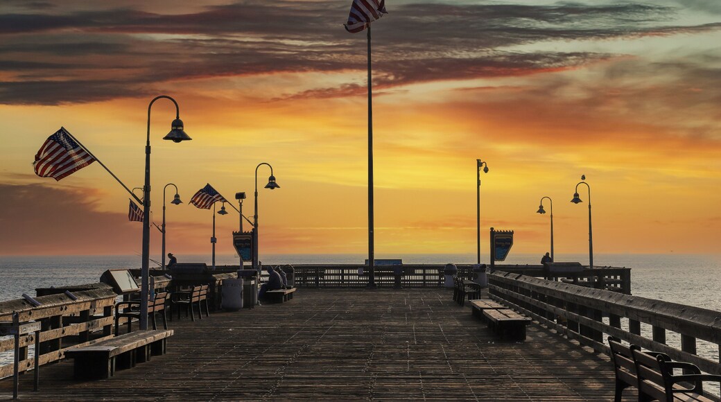 a shot of a long brown wooden pier with American flag flying on curved light posts with people fishing on the edge of the pier at sunset with powerful clouds at Ventura Pier in Ventura California USA
