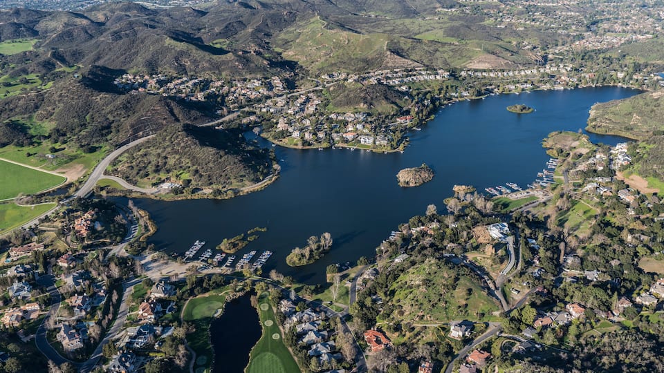An aerial view of a lake surrounded by residential areas and hilly terrain.