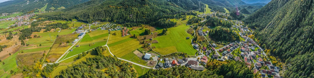 A mountainous landscape with a village nestled in the valley, surrounded by fields and forested areas.