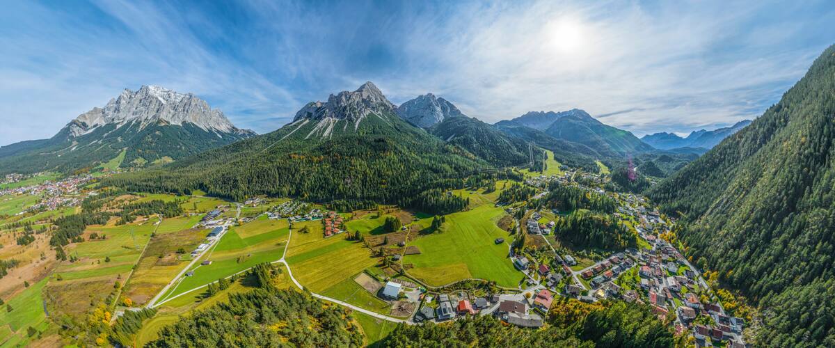 Paesaggio montuoso con un villaggio immerso nella valle, circondato da campi e aree boschive.