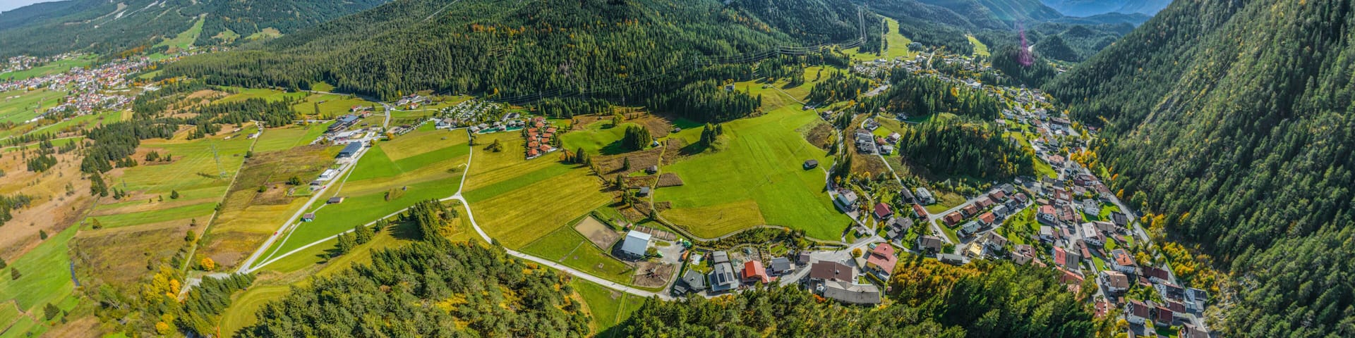 A mountainous landscape with a village nestled in the valley, surrounded by fields and forested areas.
