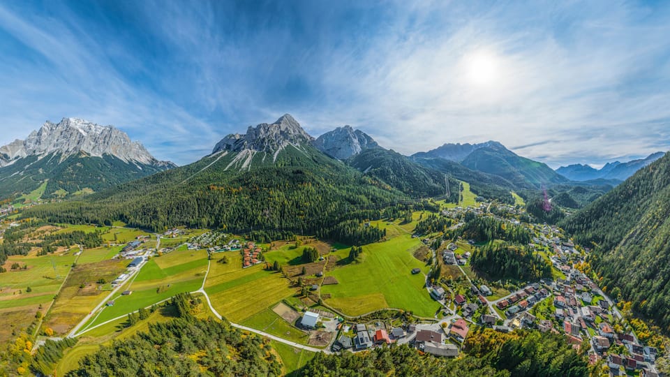 A mountainous landscape with a village nestled in the valley, surrounded by fields and forested areas.