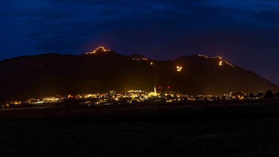 A mountain range at night with illuminated peaks and a lit-up town in the valley.
