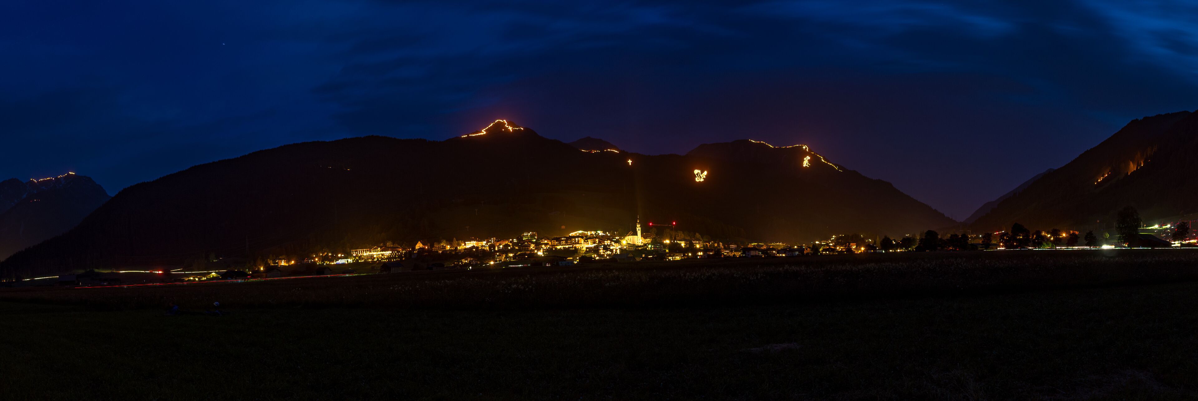A mountain range at night with illuminated peaks and a lit-up town in the valley.
