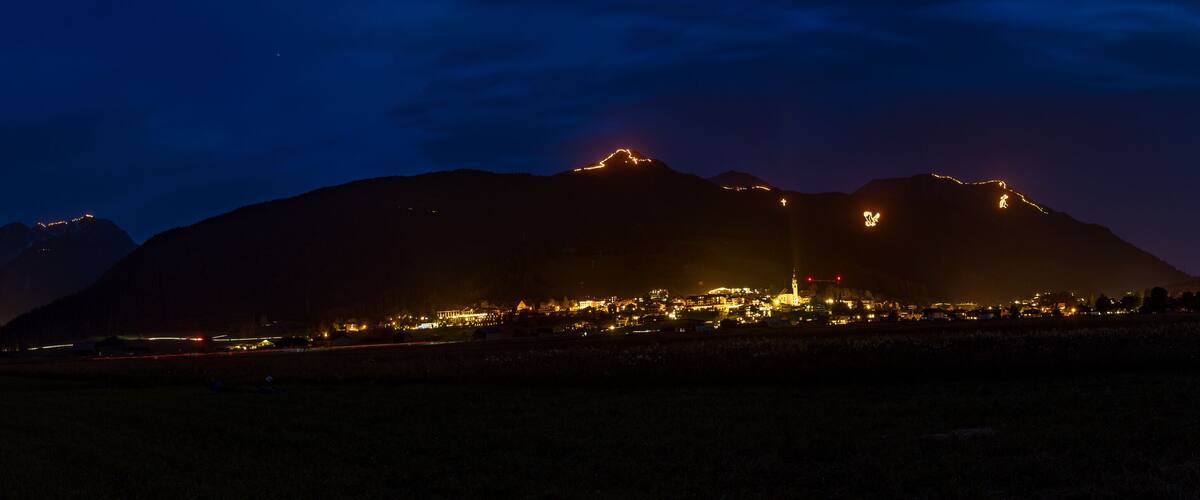A mountain range at night with illuminated peaks and a lit-up town in the valley.