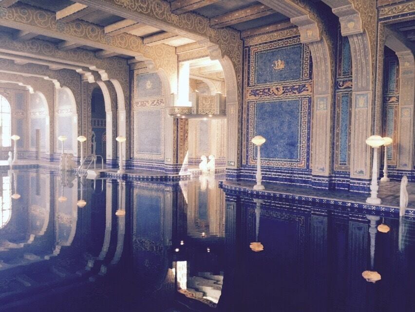 A grand hall with ornate blue and gold decorations, a polished floor reflecting the ceiling, and tall white columns.