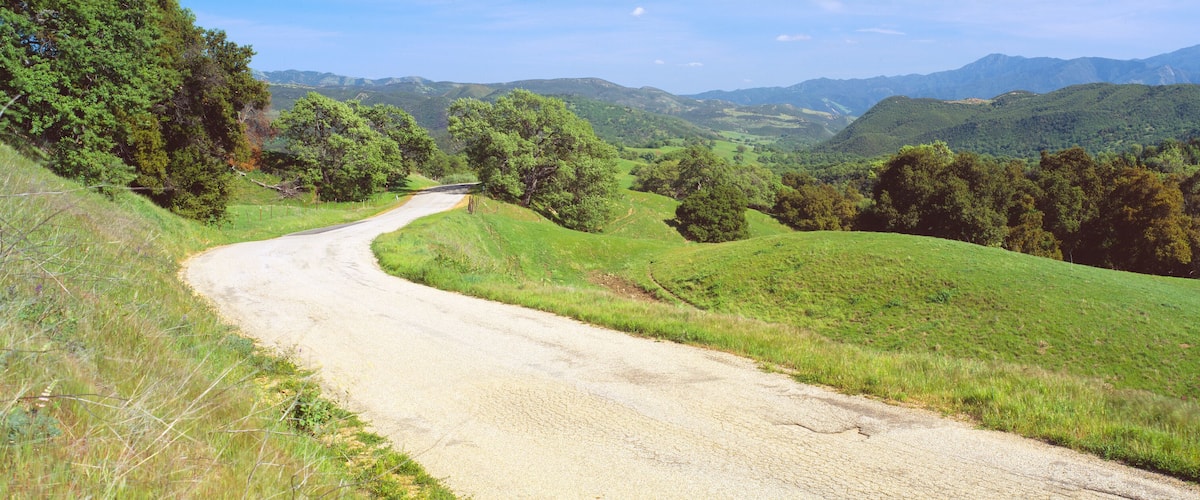 A winding dirt road through a lush green valley with rolling hills and dense forests.
