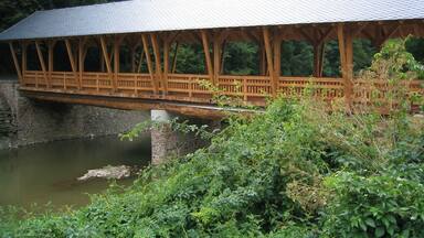 A wooden covered bridge over a river with a stone bridge in the background.
