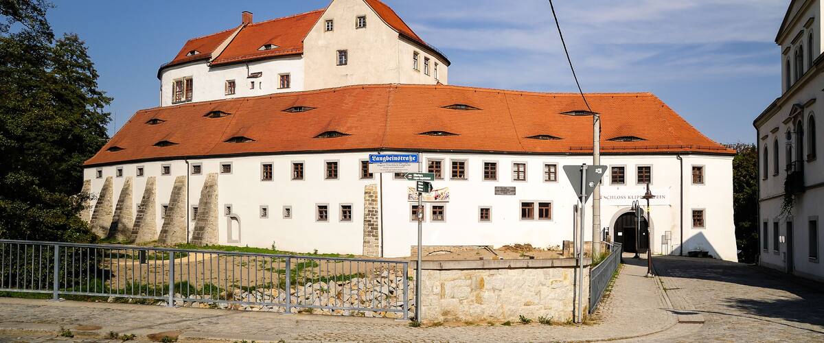 A historic building with a red-tiled roof and white walls, a stone staircase, and a sign indicating 'Schloss Klessinger'.