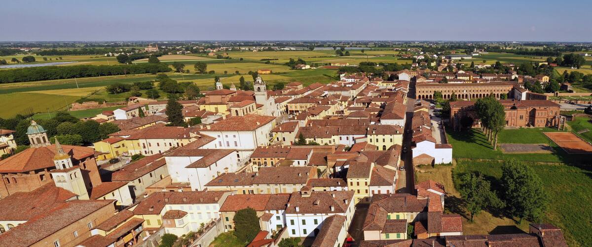 A historic town with terracotta-roofed buildings, a prominent church, and surrounding green fields.