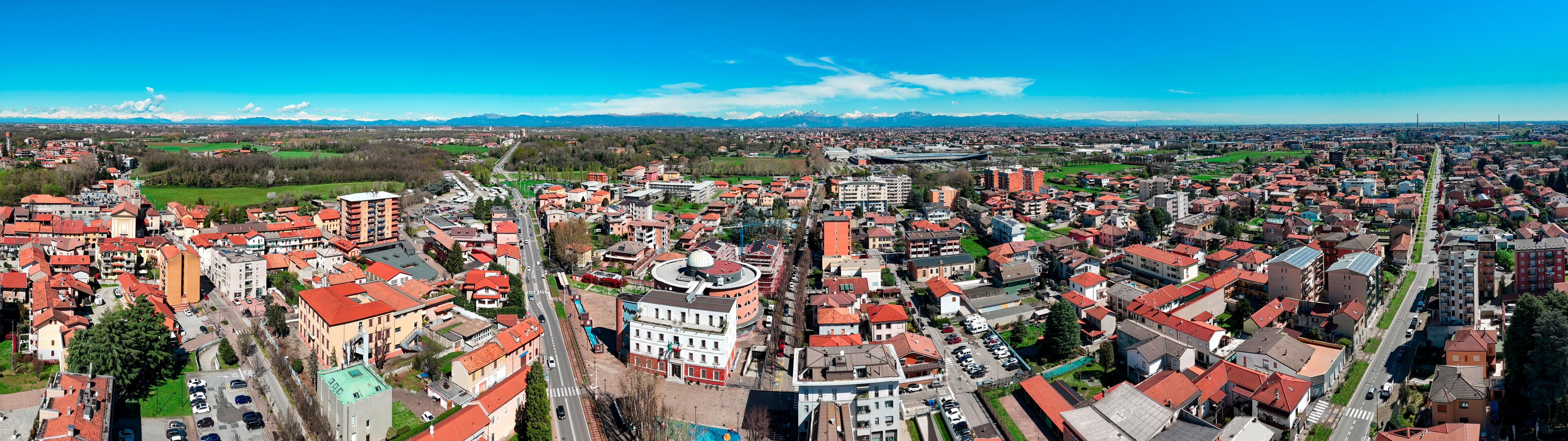 A panoramic view of a city with red-roofed buildings, a prominent church, and a mountain range in the background.