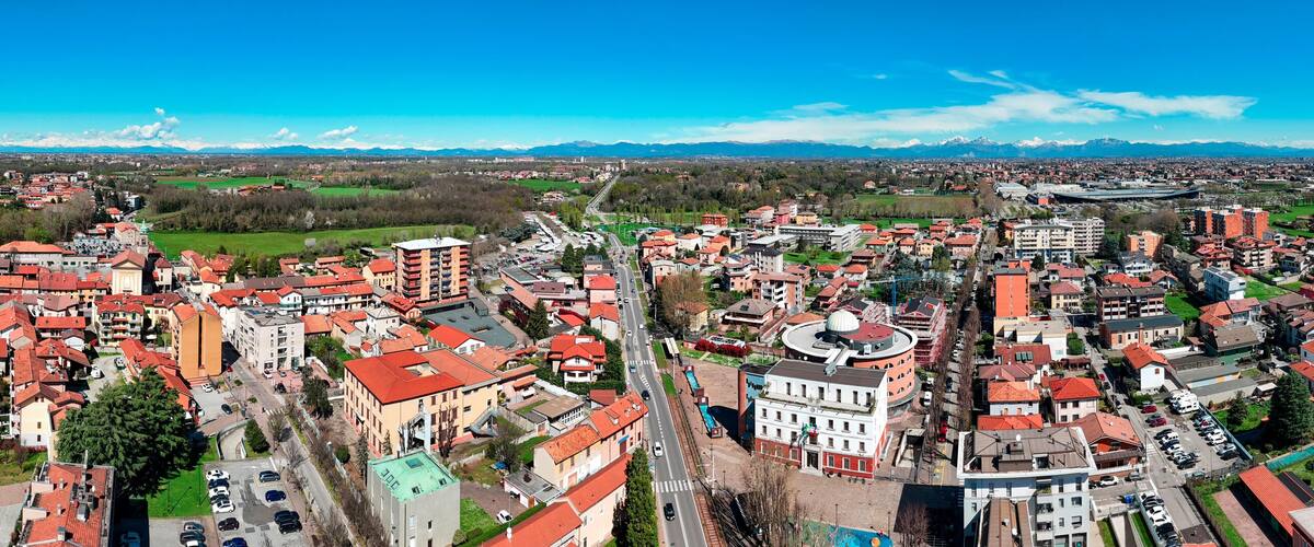 A panoramic view of a city with red-roofed buildings, a prominent church, and a mountain range in the background.