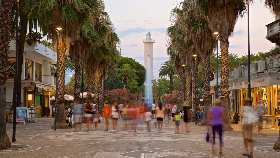 A bustling street with palm trees, a central fountain, and a tall tower in the background.