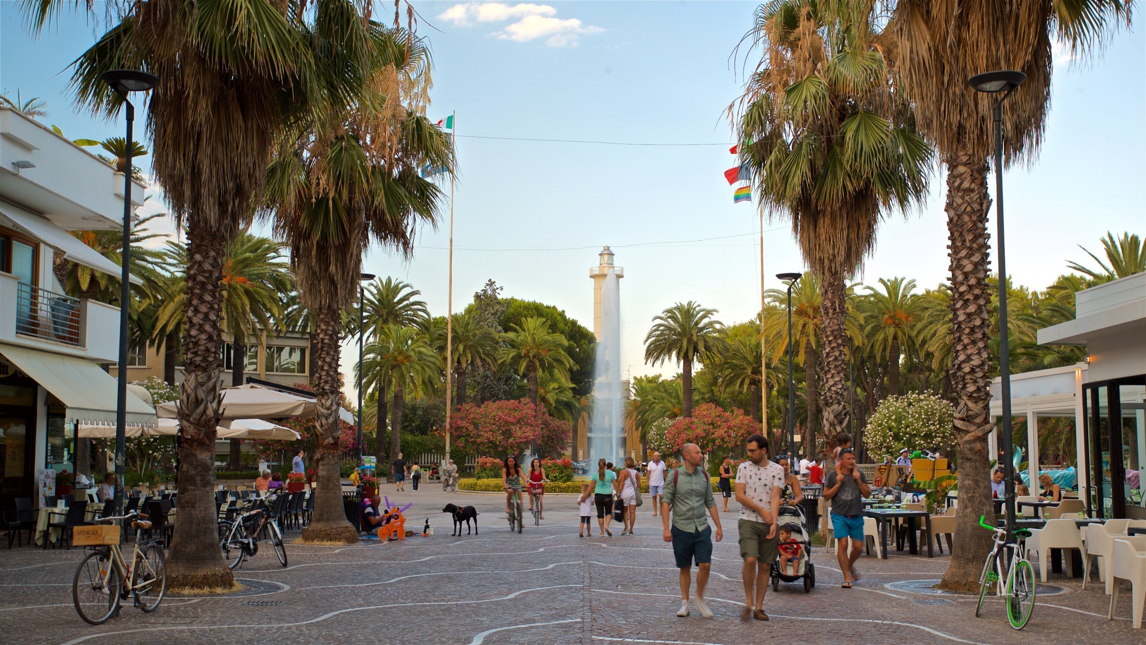 A plaza with palm trees, a fountain, and a tall monument.