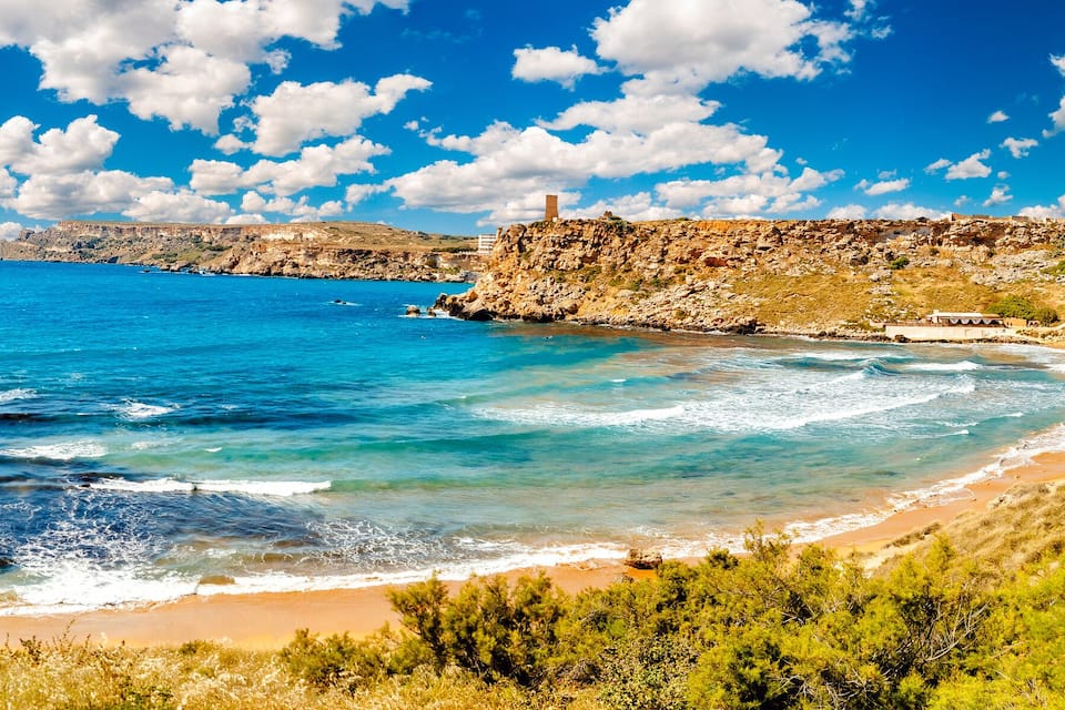 A coastal landscape with a clear blue sea, rocky cliffs, and a sandy beach.