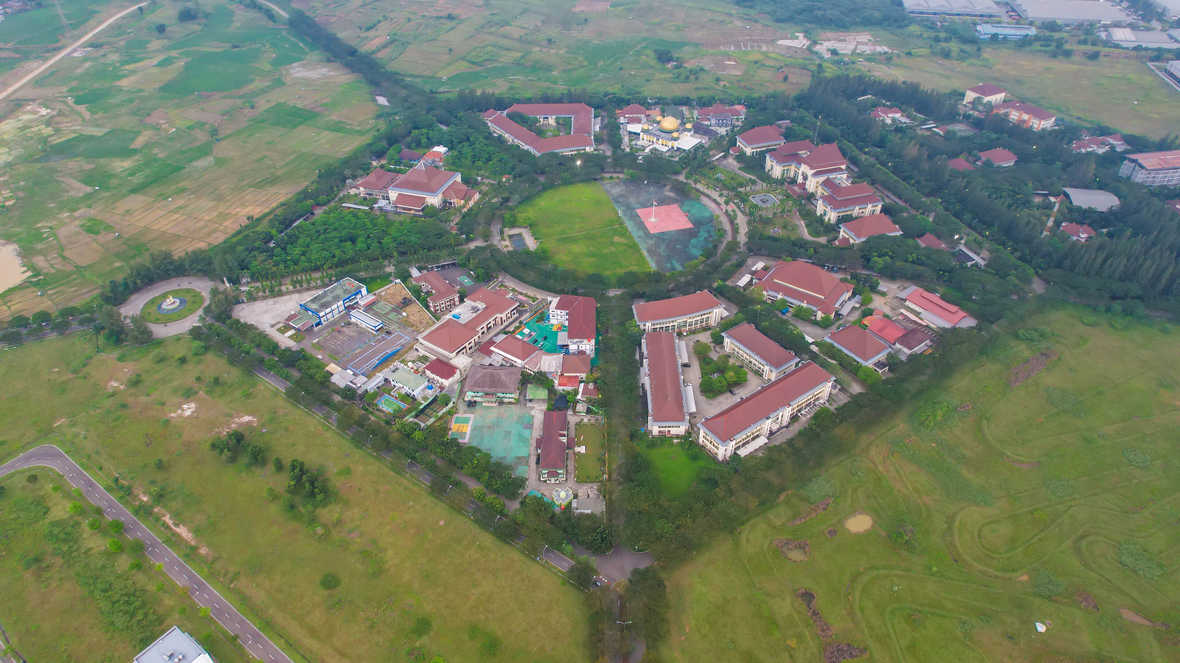 An aerial view of a residential area with houses, a central green space, and surrounding fields.