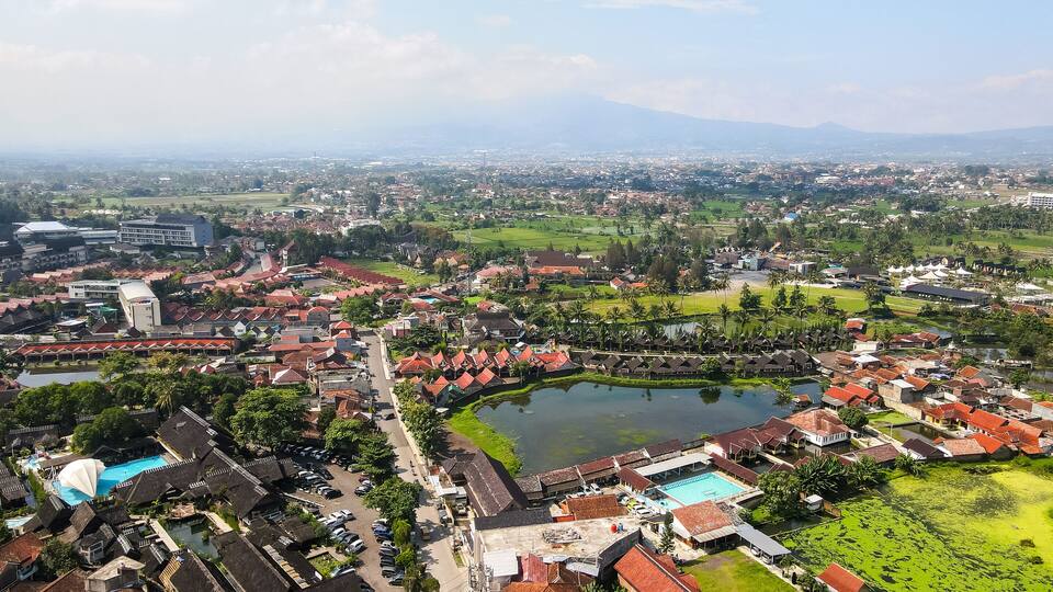 An aerial view of a town with a central lake, surrounded by residential buildings and greenery.