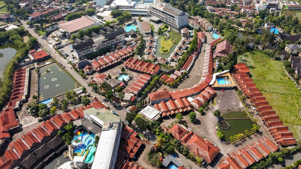 An aerial view of a coastal town with red-roofed buildings, a large swimming pool, and a marina.