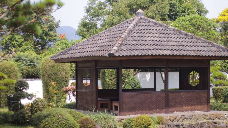 A traditional Japanese pavilion with a tiled roof, surrounded by lush greenery and a small pond.