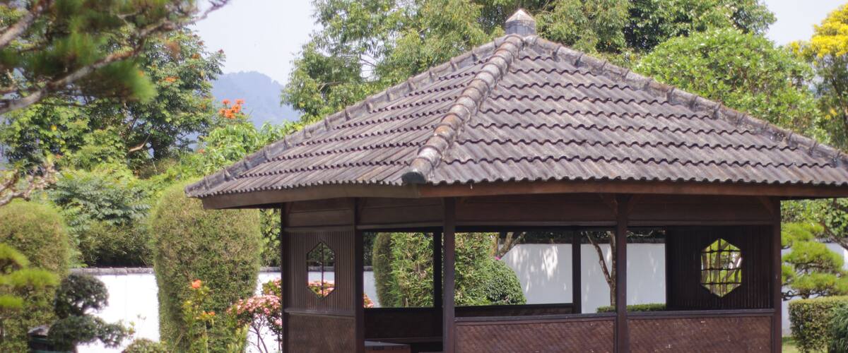 A traditional Japanese pavilion with a tiled roof, surrounded by lush greenery and a small pond.