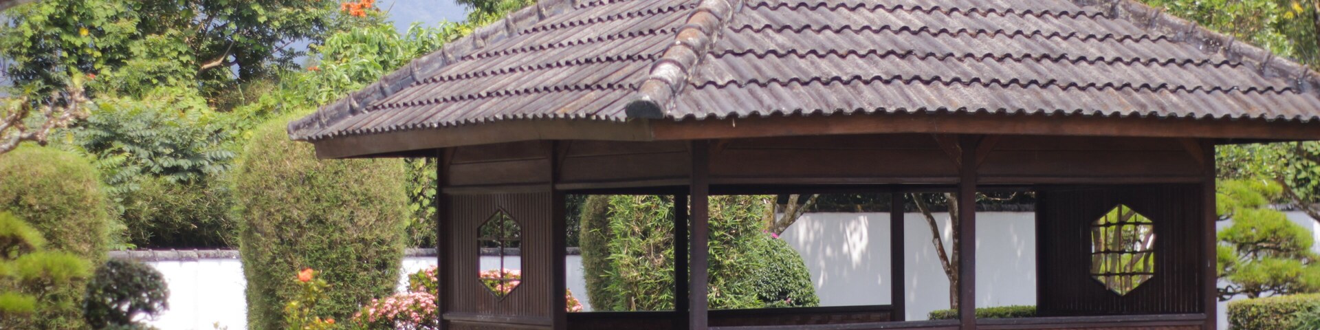 A traditional Japanese pavilion with a tiled roof, surrounded by lush greenery and a small pond.