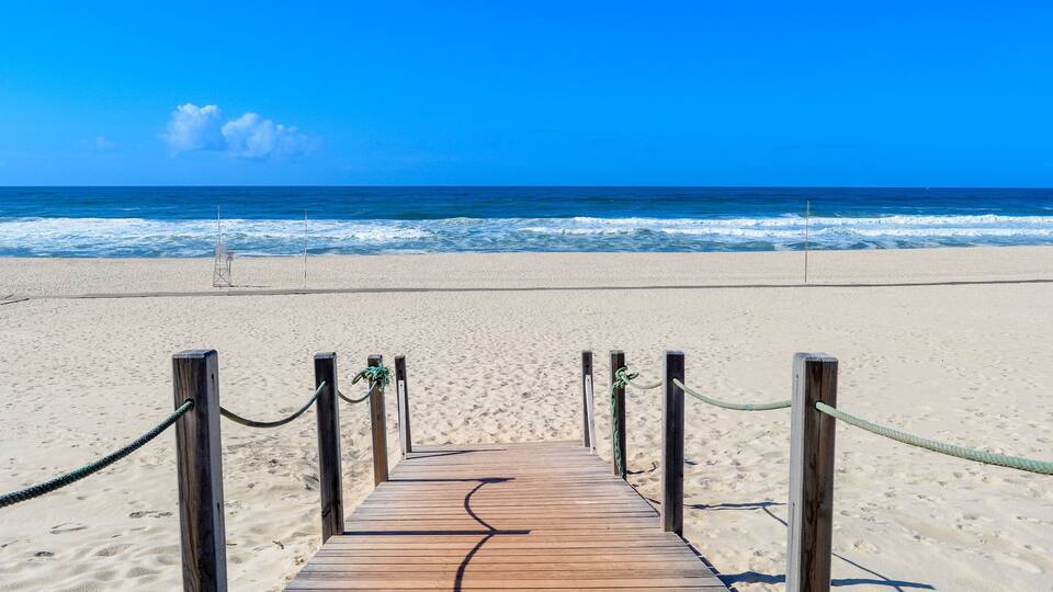 A wooden boardwalk leading to a beach with a clear blue sky and ocean waves.