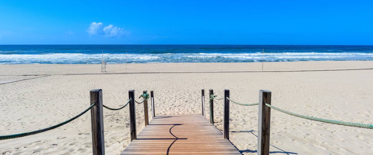 A wooden boardwalk leading to a beach with a clear blue sky and ocean waves.