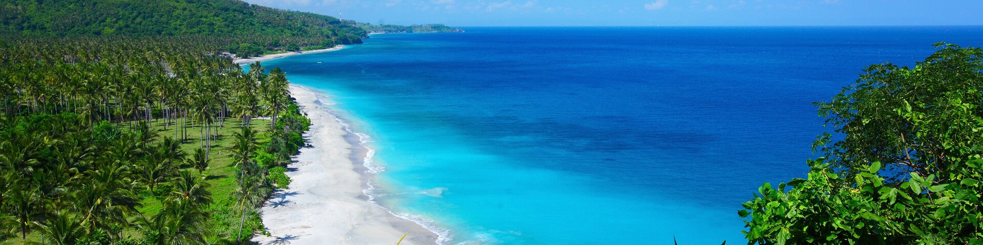Tropical lagoon with clear water and beach with white sand and palm trees in a valley. Lombok island, Indonesia