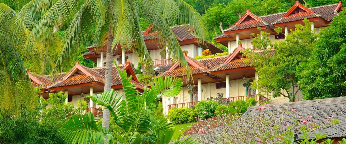 A traditional multi-story building with red-tiled roofs, surrounded by lush greenery and palm trees.
