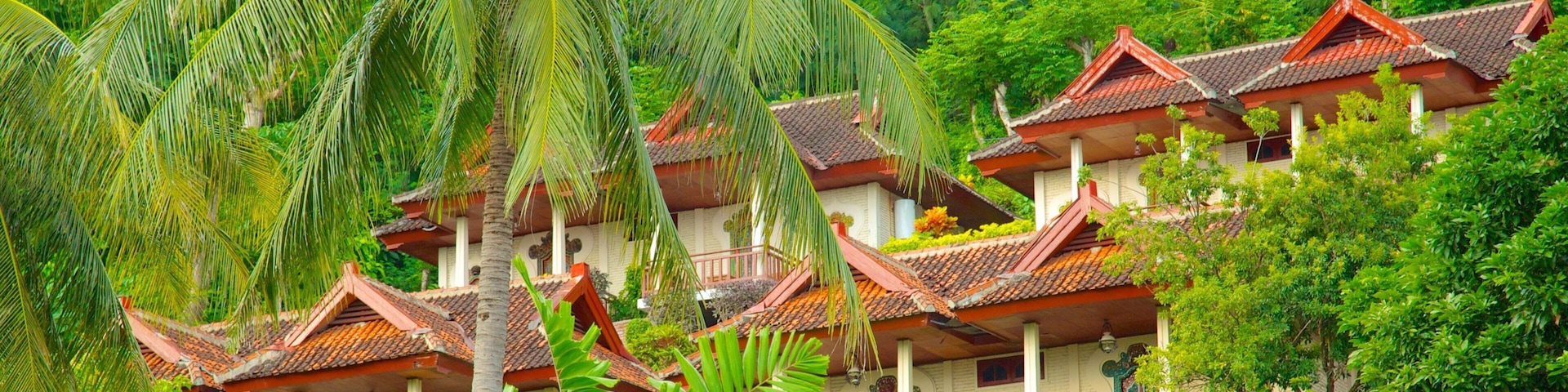A traditional multi-story building with red-tiled roofs, surrounded by lush greenery and palm trees.