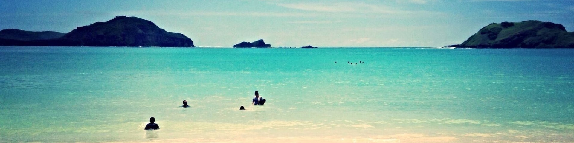 Uma praia com águas turquesa cristalinas, areal arenoso e ilhas ao longe.