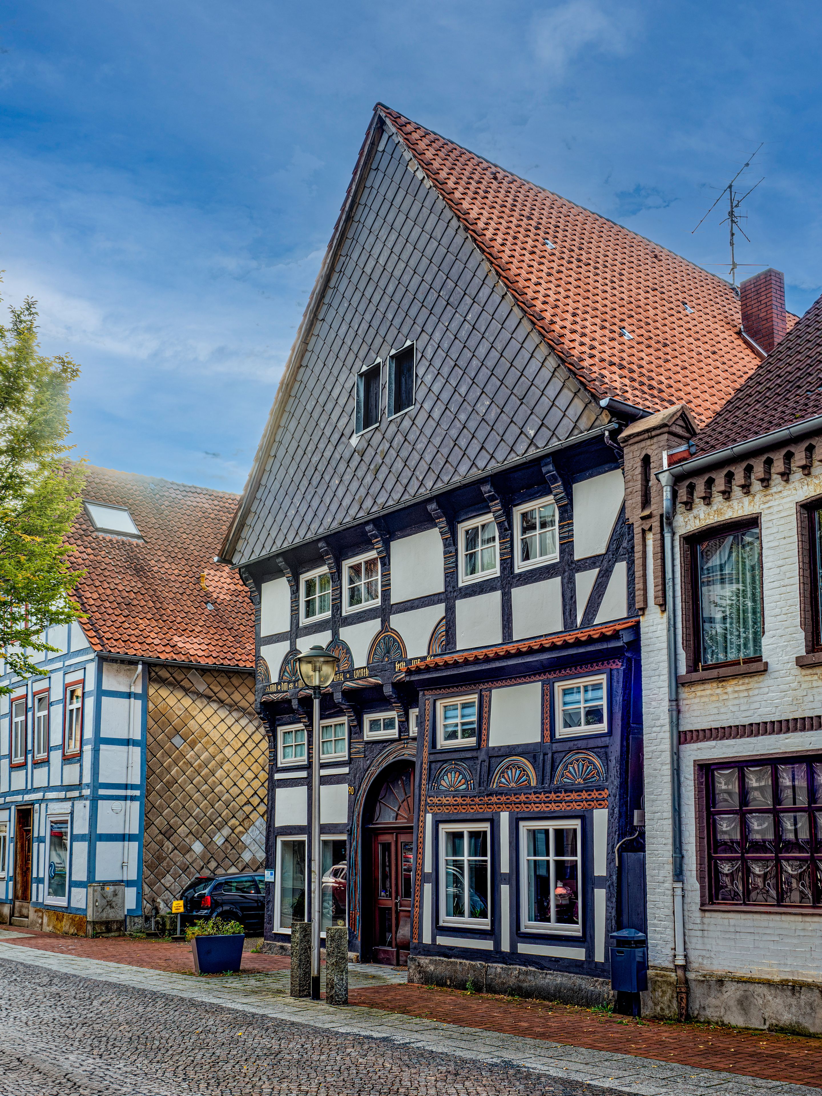 A traditional half-timbered house with a steeply pitched roof, a visible chimney, and a street lamp.