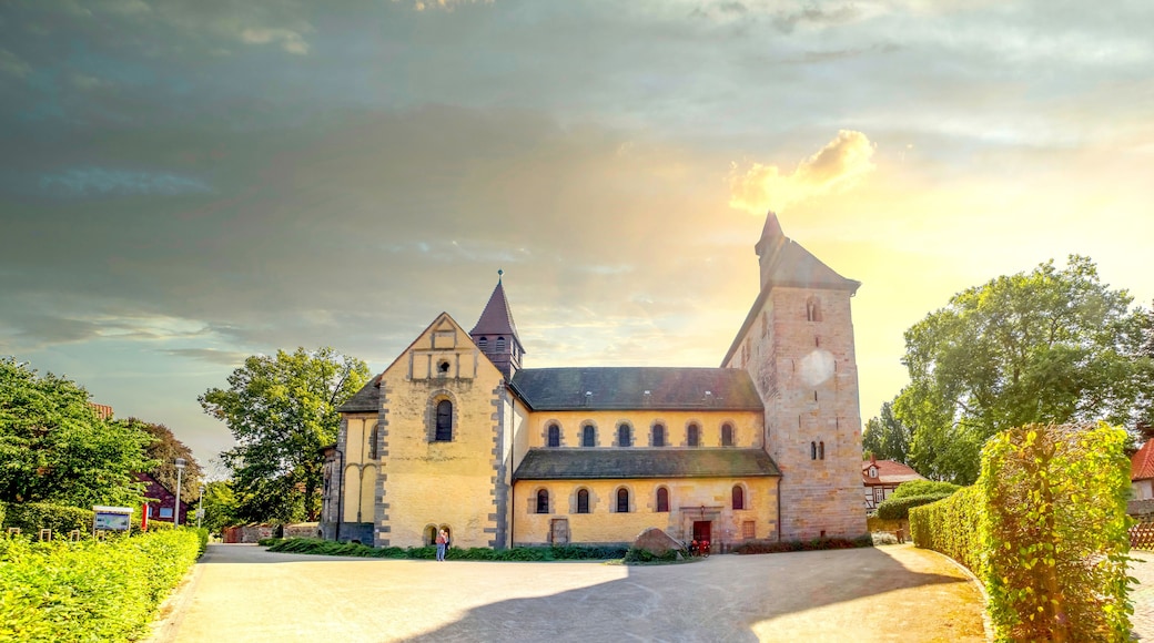 A historic church with a prominent tower and a smaller adjacent building, surrounded by lush greenery and a paved driveway.